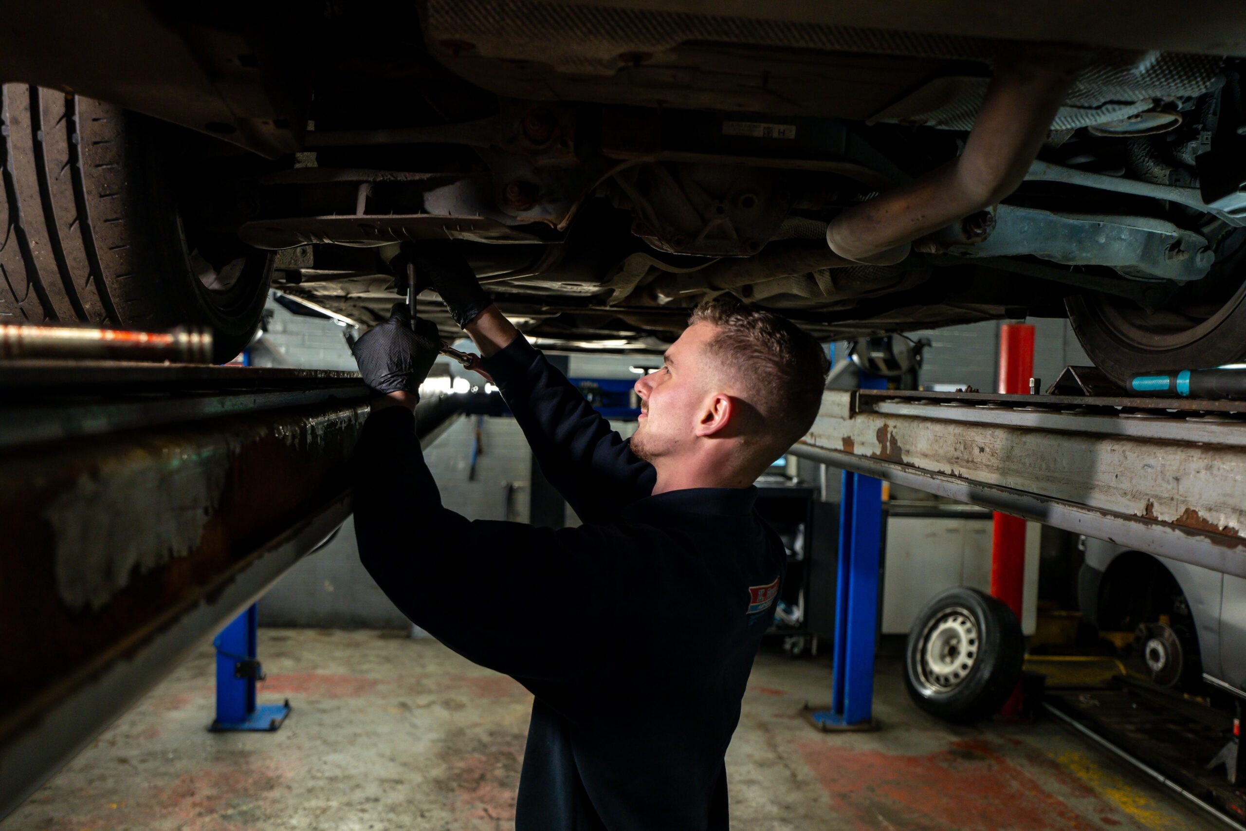 Mechanic working under car up on a ramp at K Brown Auto Repairs 