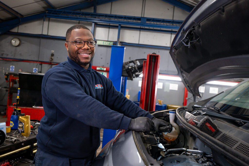 Mechanic standing over engine bay smiling